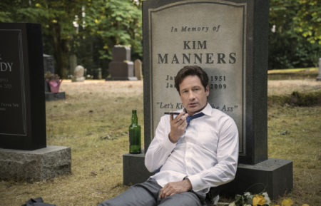 David Duchovny talking on his phone in front of the gravestone of Kim Manners in The X-Files