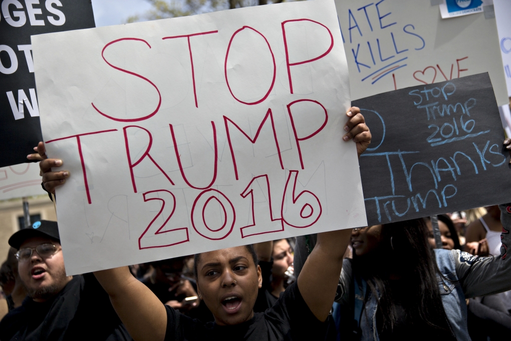 A demonstrator holds a "Stop Trump 2016" sign while chanting towards attendees waiting in line across the street for a rally with Donald Trump, president and chief executive of Trump Organization Inc. and 2016 Republican presidential candidate, at West Chester University in West Chester, Pennsylvania, U.S., on Monday, April 25, 2016. In a move that may be too little too late, Trump's two remaining opponents for the Republican presidential nomination, Ted Cruz and John Kasich, have cut a deal to play in certain states and avoid others in an effort to stop dividing the anti-Trump vote. Photographer: Andrew Harrer/Bloomberg via Getty Images