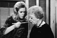 American actress Elizabeth Montgomery (1933 - 1995) (left, as Samantha Stephens) feeds American actress Marion Lorne (1883 - 1968) (as Aunt Clara) with a wooden cooking spoon as she holds a cookbook entitled 'Sukiyaki: the art of Japanese cooking' in a still from the episode 'A Majority of Two' of the television sitcom 'Bewitched,' April 11, 1968.