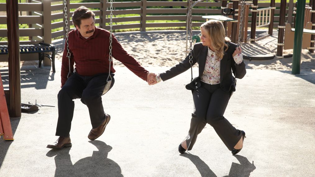 Nick Offerman as Ron Swanson and Amy Poehler as Leslie Knope holding hands on a swing in Parks and Recreation - Season 7