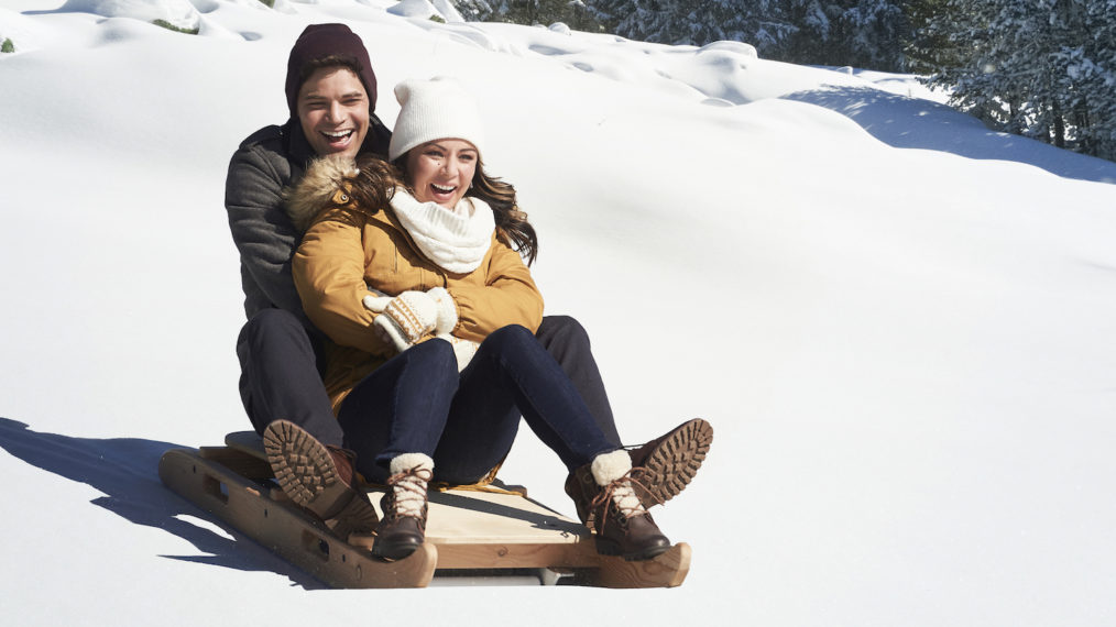 Jeremy Jordan and Janel Parrish riding a sled in Holly and Ivy