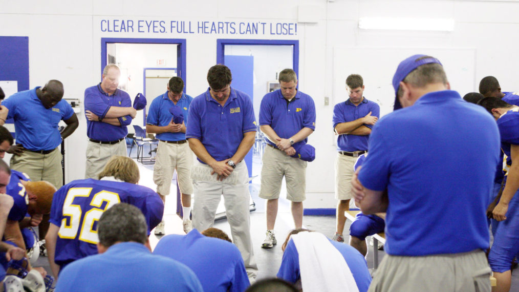 Kyle Chandler as Coach Taylor bowing head in prayer in Friday Night Lights