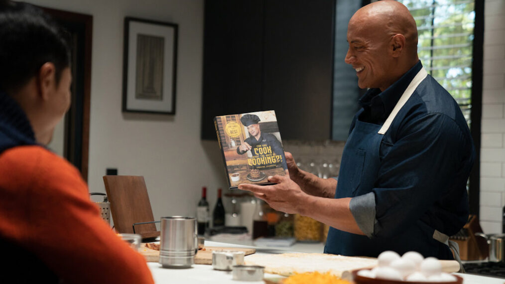 Dwayne Johnson in Young Rock holding up his cookbook