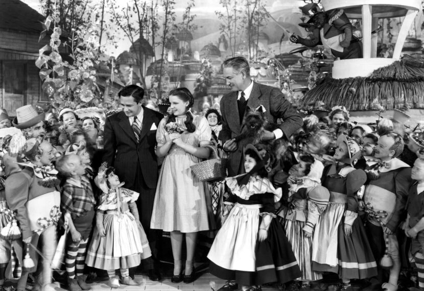 Producer Mervyn LeRoy, star Judy Garland and director Victor Fleming posing with actors, on set of Wizard of Oz