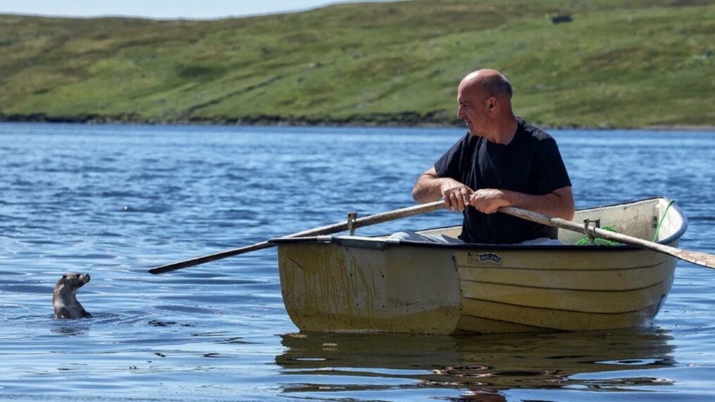 A man rows a boat in a river with an otter watching nearby in 'Billy and Molly: An Otter Love Story'