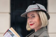 Lucy Worsley in deerstalker hat and book in hand in front of the 221B Baker Street door