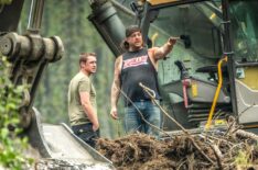 Rick Ness and Bailey Carten mid conversation by excavator, busy foreground in Gold Rush