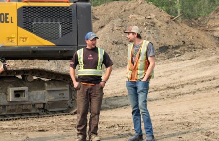 Mitch Blaschke and Parker Schnabel stood chatting next to excavator, 