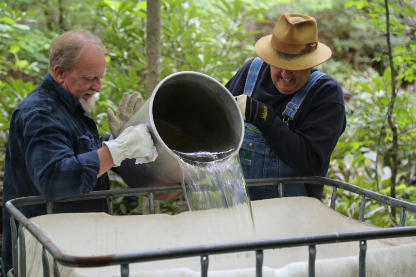 Eric "Digger" Manes and Mark Ramsey pour water into a large tote in the woods.