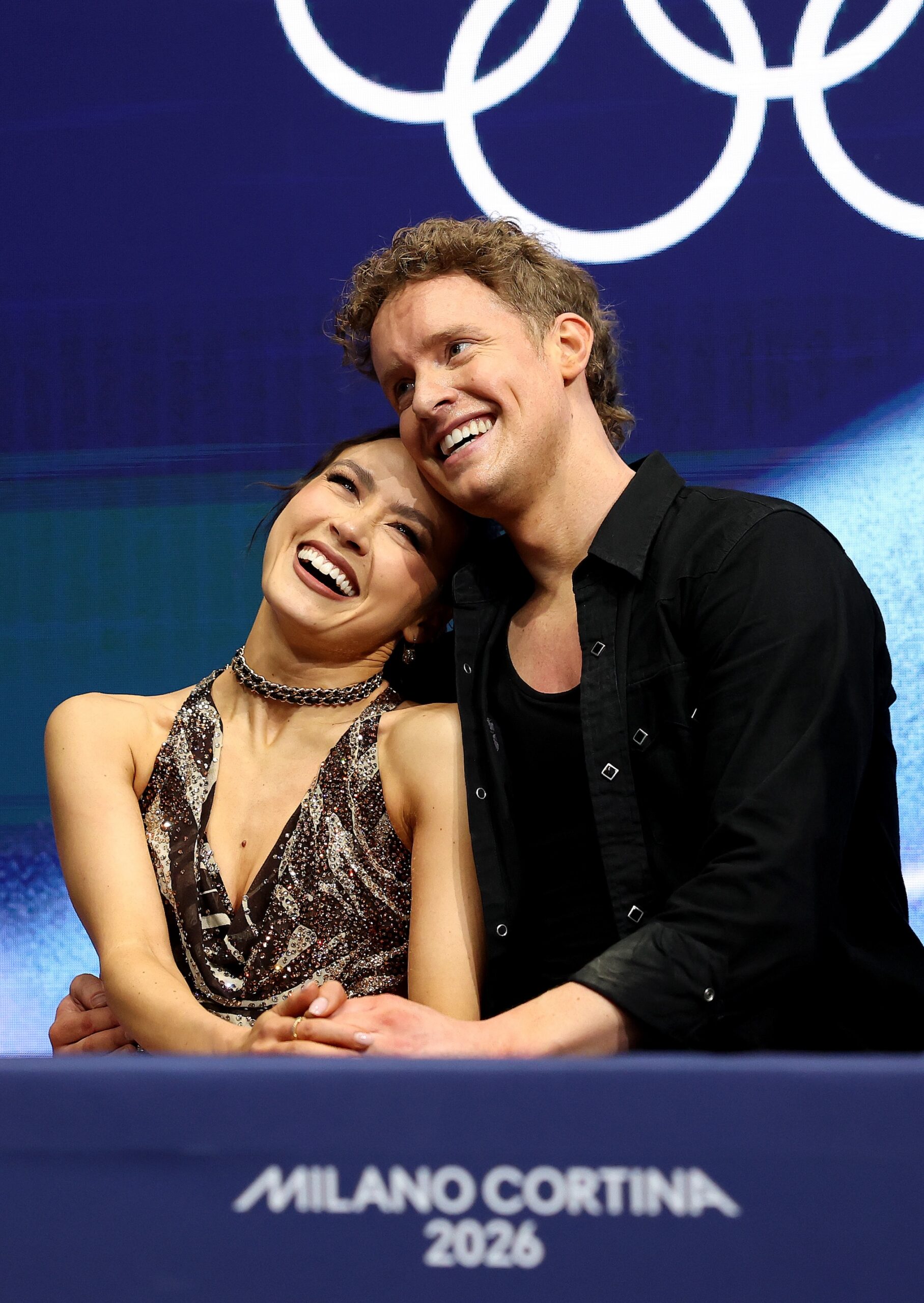 Madison Chock and partner Evan Bates of Team United States react with their team in the Kiss and Cry zone after competing in Ice Dance - Rhythm Dance Qualification on day three of the Milano Cortina 2026 Winter Olympic games at Milano Ice Skating Arena on February 09, 2026 in Milan, Italy.