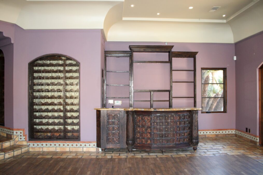 Bar counter, shelving wall, arched window, interior wide shot, pre-makeover, as seen on Bachelor Mansion Takeover, Season 1.