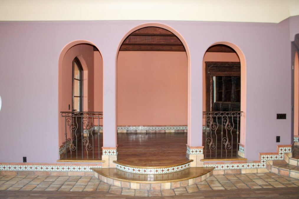 Wide shot of empty rose-colored room showing arched doors, fireplace, and wood floor in pre-makeover, as seen on Bachelor Mansion Takeover, Season 1.