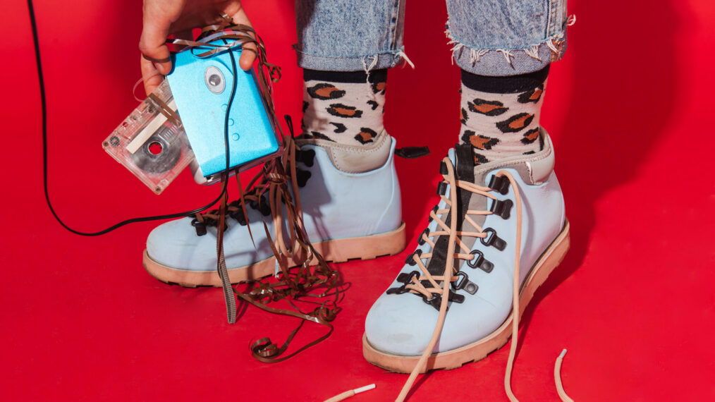 Retro styled fashionable woman in sport jacket and jeans with vintage cassette player on red background. Fashion back to 80s - 90s new trend concept
