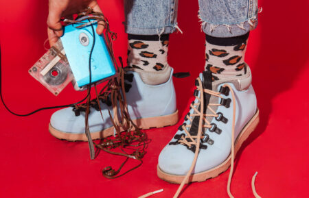 Retro styled fashionable woman in sport jacket and jeans with vintage cassette player on red background. Fashion back to 80s - 90s new trend concept