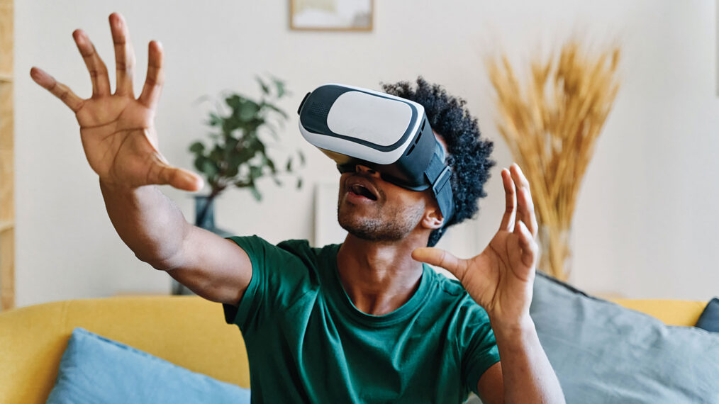 Man sitting on apartment living room couch wearing augmented reality glasses moving his hands while feeling like he is inside the simulation.