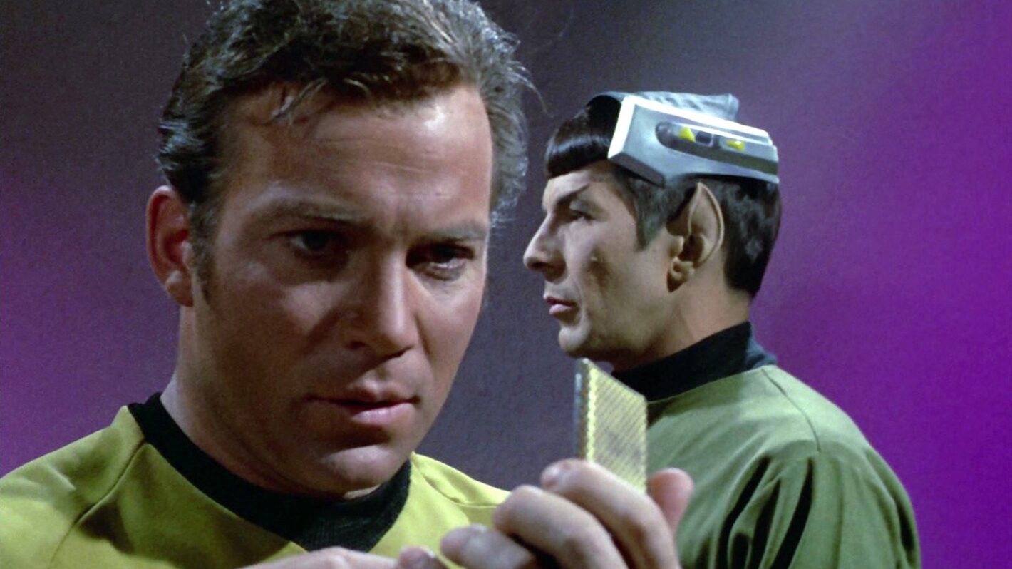 William Shatner as Captain James T. Kirk speaks into his communicator with Leonard Nimoy as Mr. Spock in the background in 'Star Trek' Season 3 Episode 1, 'Spock's Brain'